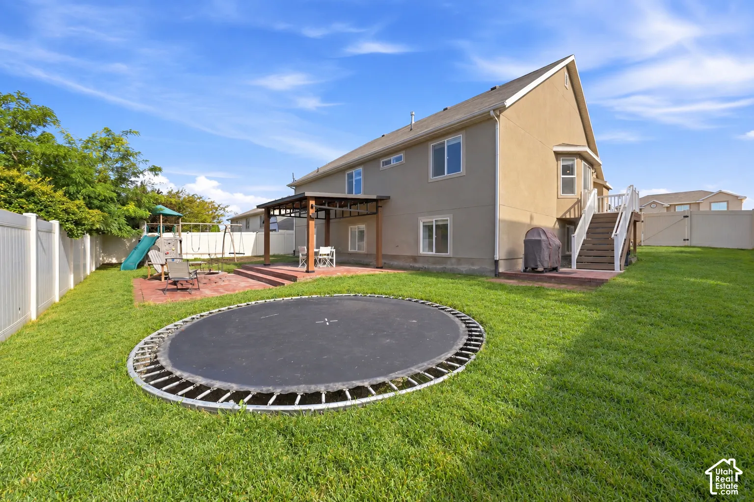 Expansive backyard with a manicured lawn, white privacy fencing, a ground-level patio, and a covered outdoor structure