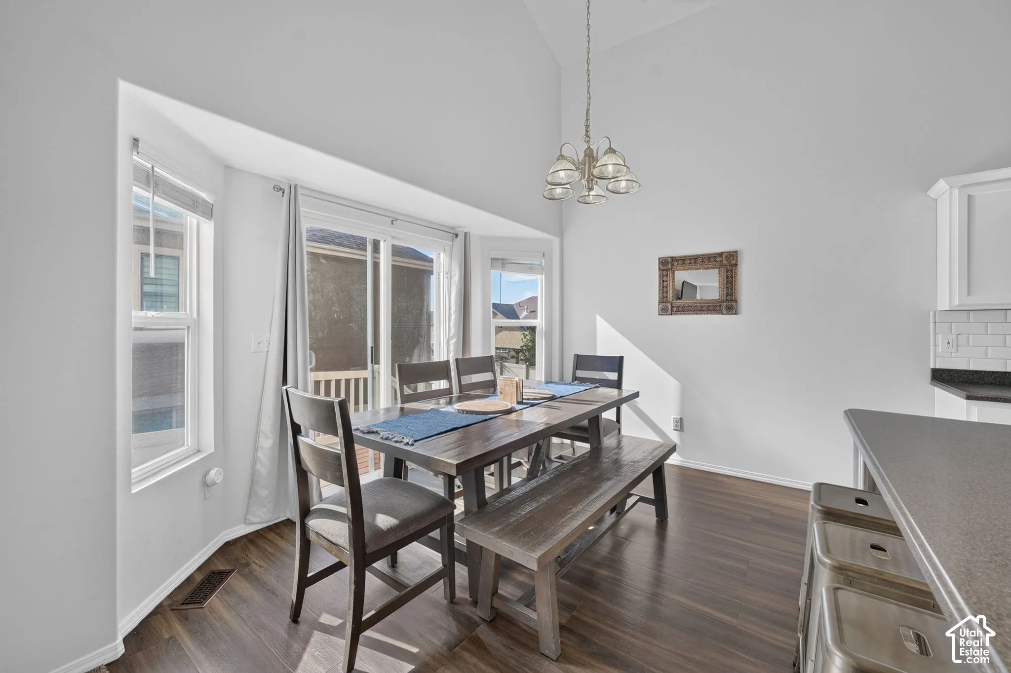 Vaulted ceiling with an attached chandelier, wood-finish flooring, bay window, sliding glass door, and white subway tile backsplash