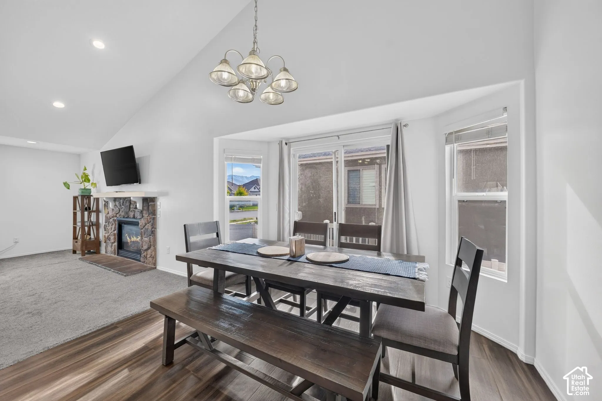 Vaulted ceiling with an industrial-style chandelier, stone-clad fireplace, wood-finish flooring, and recessed lighting