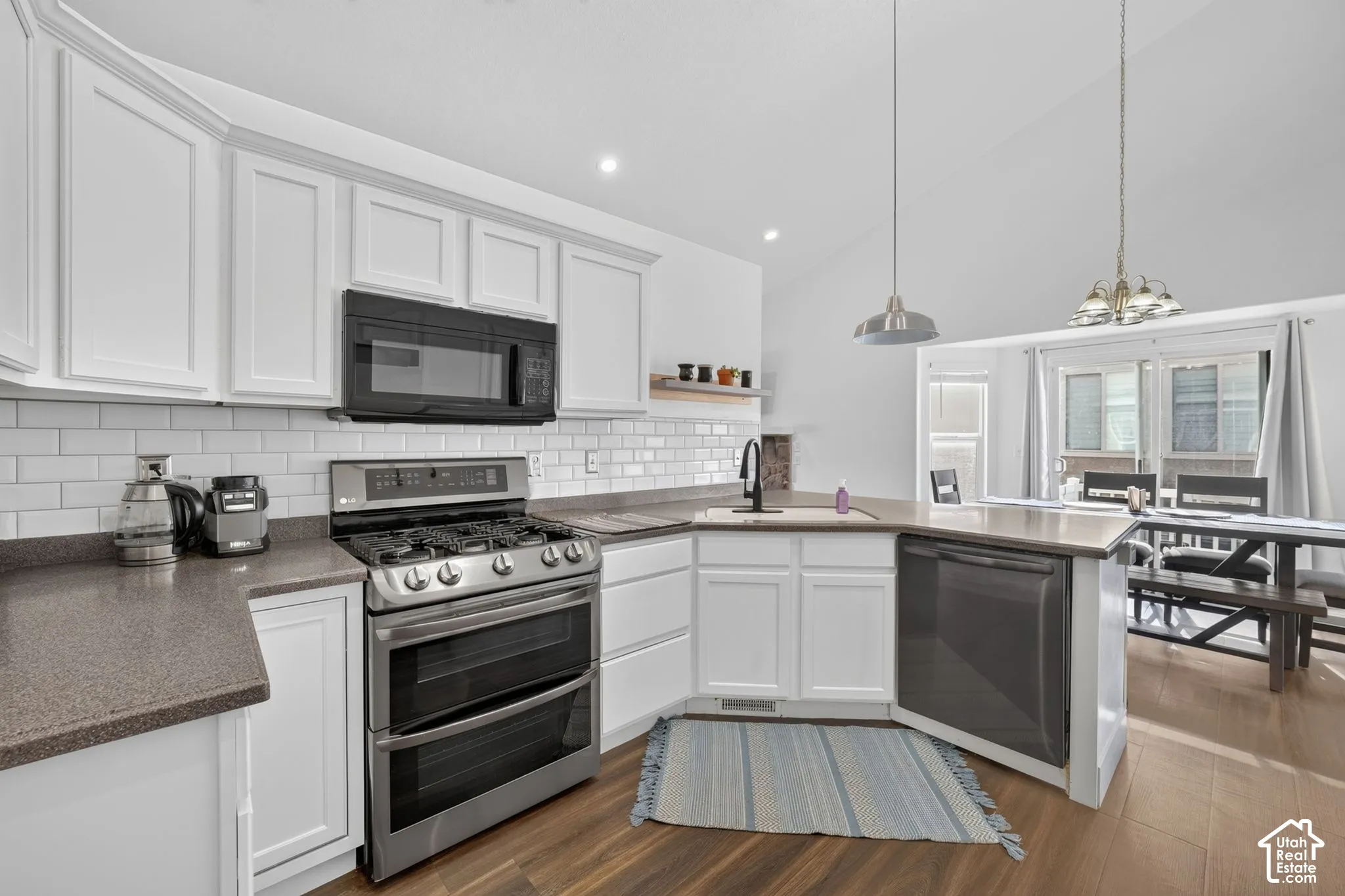 Modern kitchen featuring white cabinetry with recessed panel detailing, stainless steel gas range with dual ovens, stainless steel dishwasher, subway tile backsplash, quartz countertops, and wood-finish flooring throughout