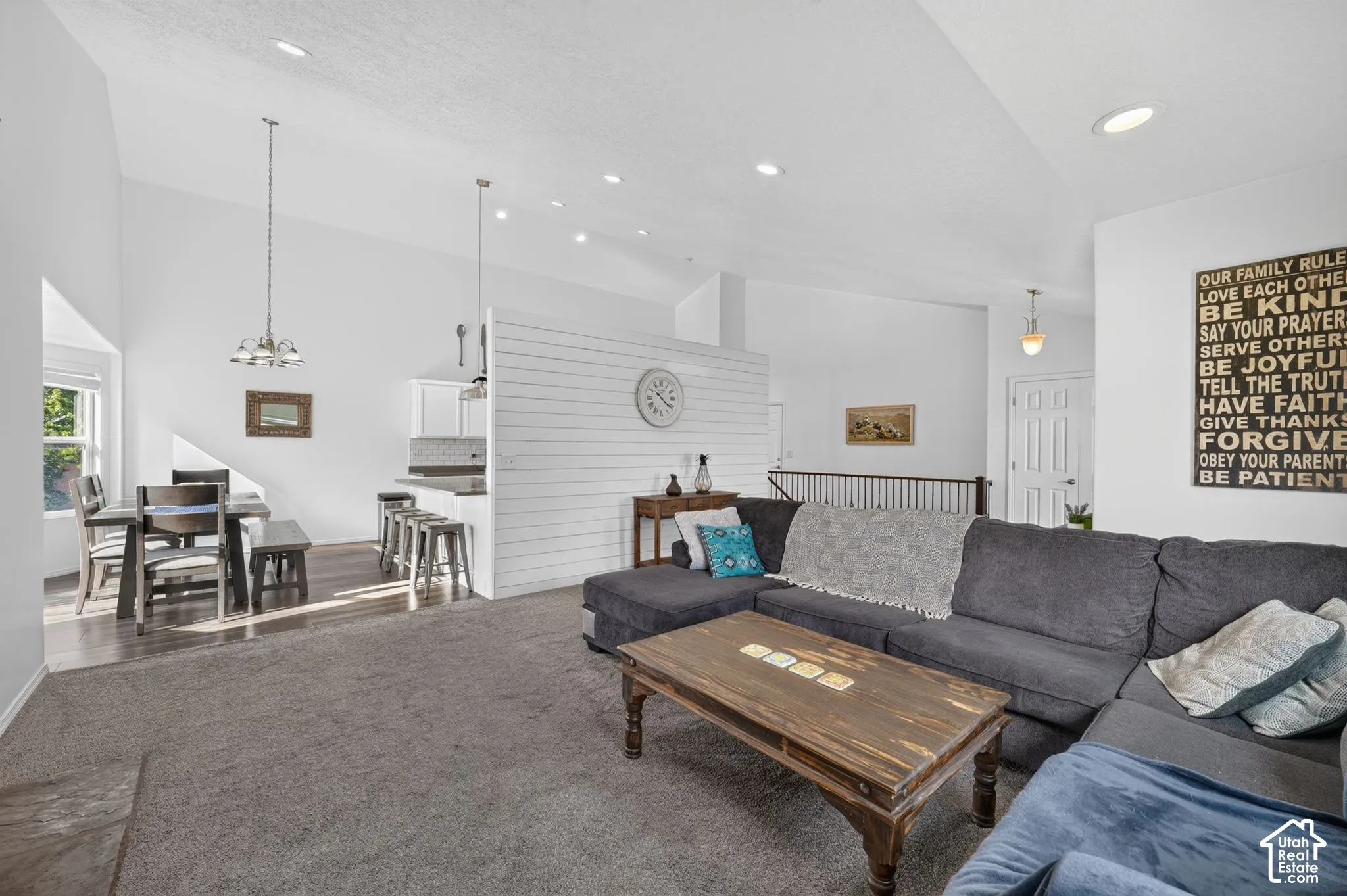Vaulted ceiling, recessed lighting, wood-finish flooring, kitchen island with counter seating, and a decorative shiplap accent wall