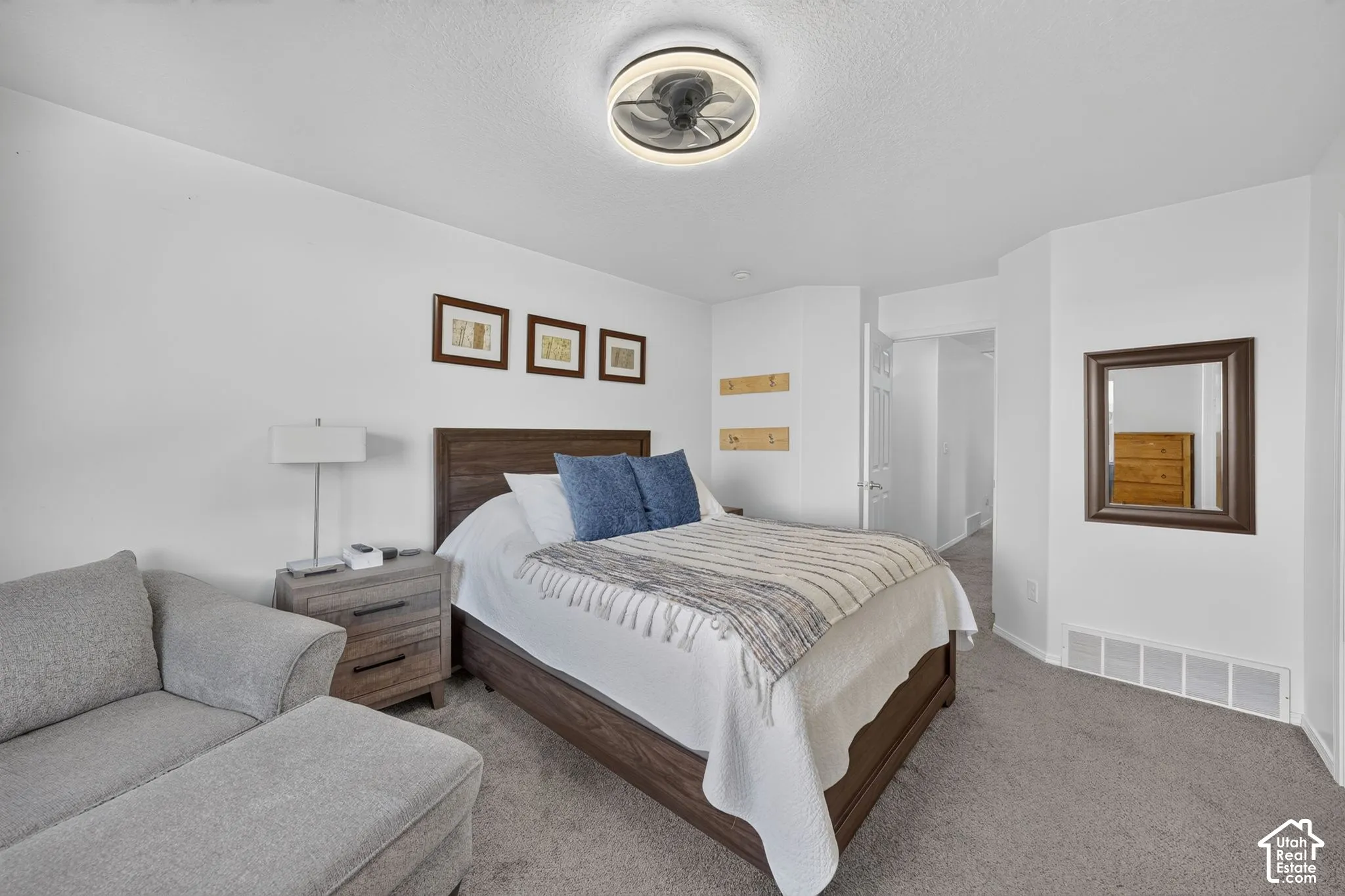 Spacious bedroom offering a wood-finish bed frame, carpeted flooring, and soft white bedding