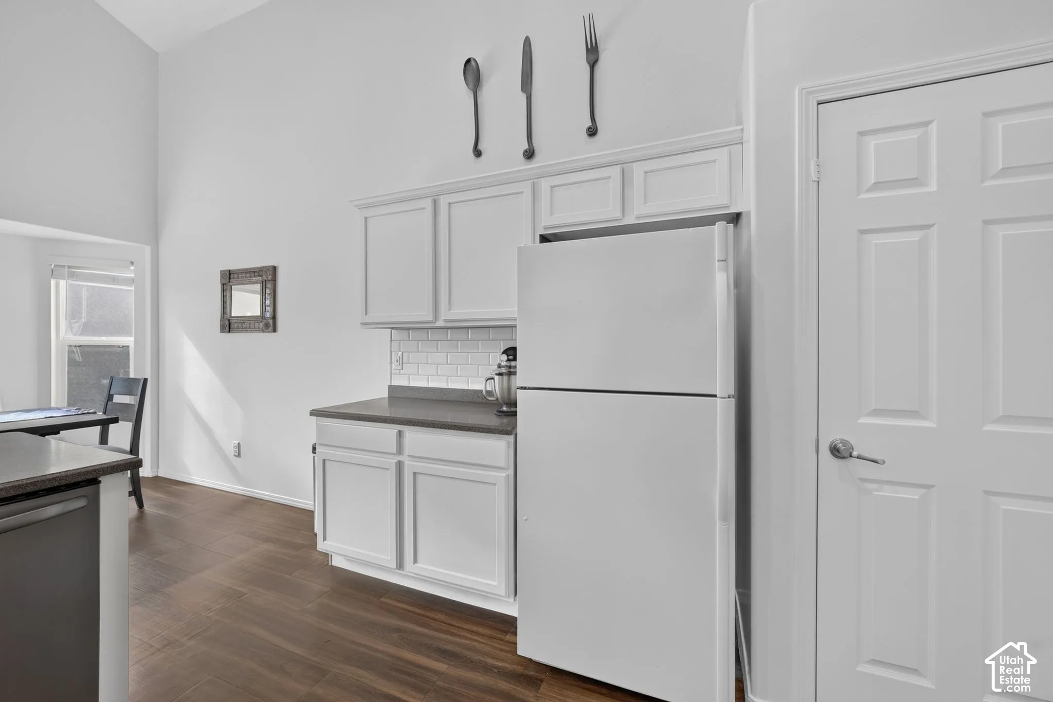 Efficient kitchen featuring white cabinetry with recessed-panel doors, stainless steel refrigerator, and a subway tile backsplash