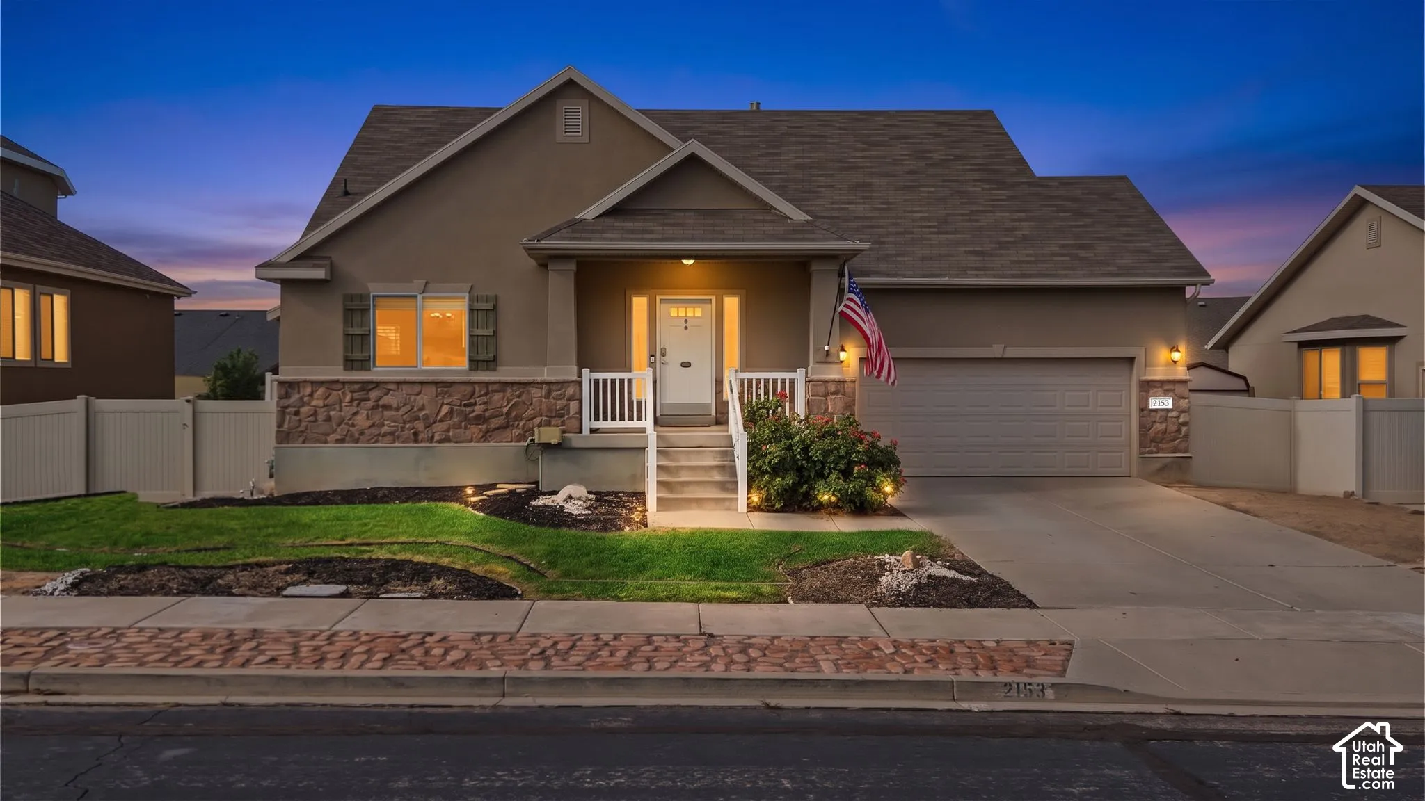Stucco exterior with stone accent, covered front porch, concrete driveway, attached garage, and landscaped front yard