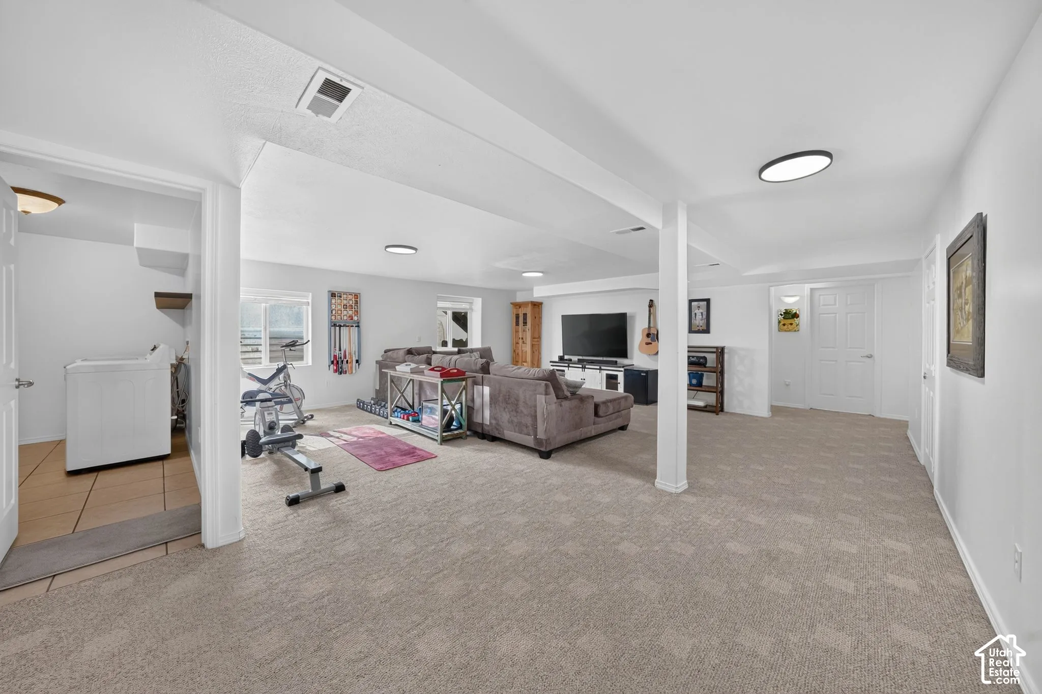 Expansive finished space featuring carpeted flooring, recessed lighting, and a dedicated laundry area with tiled flooring