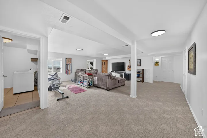 Expansive finished space featuring carpeted flooring, recessed lighting, and a dedicated laundry area with tiled flooring