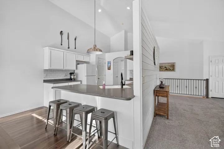 Kitchen island with seating, white shaker-style cabinetry, subway tile backsplash, and wood-finish flooring