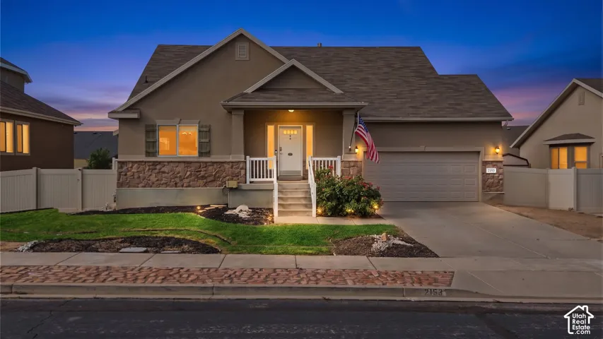 Stucco exterior with stone accent, covered front porch, concrete driveway, attached garage, and landscaped front yard