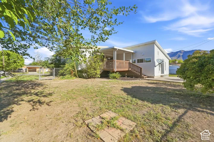 Rear exterior featuring a covered wood deck, wood railings, and a concrete patio