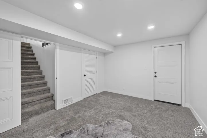 Recessed lighting illuminates the carpeted flooring and white walls