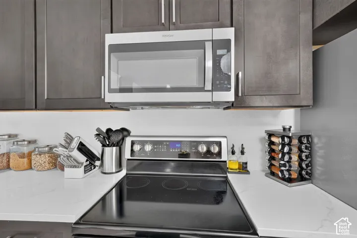 Stainless steel microwave and range, dark wood-finish cabinetry, and white countertops