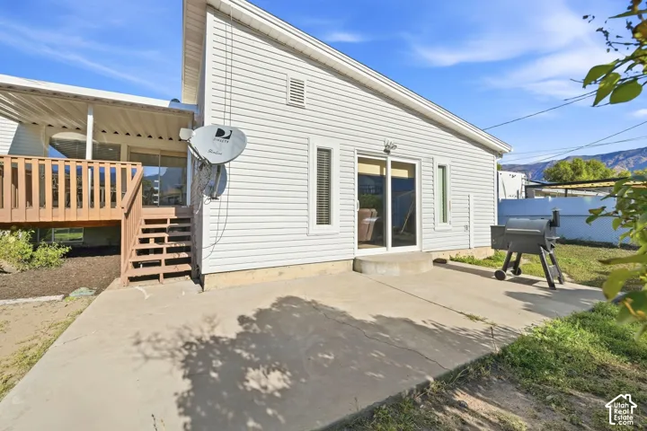 Rear exterior featuring a covered wood deck, wood stairs, concrete patio, and sliding glass door