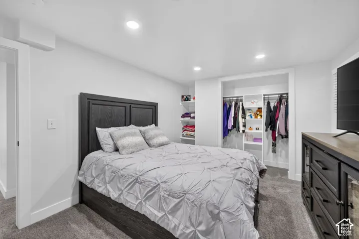 Recessed lighting, wood-finish bed frame, carpet flooring, built-in closet organization, and white trim