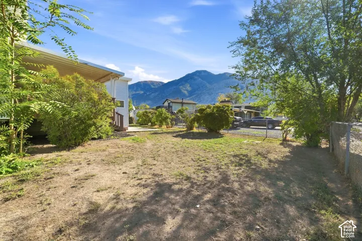 Expansive outdoor area featuring mature trees, a chain link fence, and mountain scenery