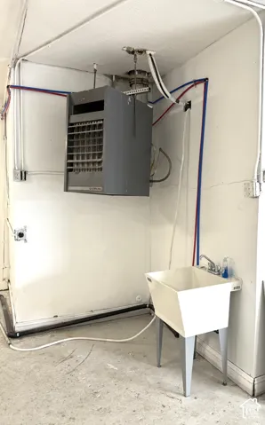Wall-mounted utility heater, exposed conduit, surface-mounted electrical outlets, and a freestanding utility sink