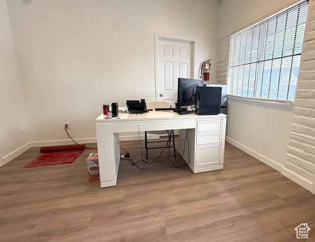 Wood-finish flooring, white paneling, textured brick wall, white blinds, and white trim