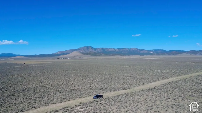 Expansive open land featuring natural desert vegetation, a visible dirt road, and distant mountain ranges