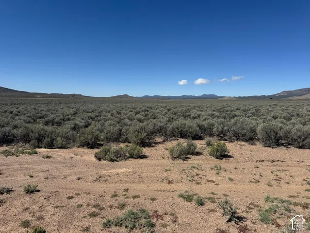 Expansive natural landscape featuring desert brush, open terrain, and distant mountain ranges under a clear sky