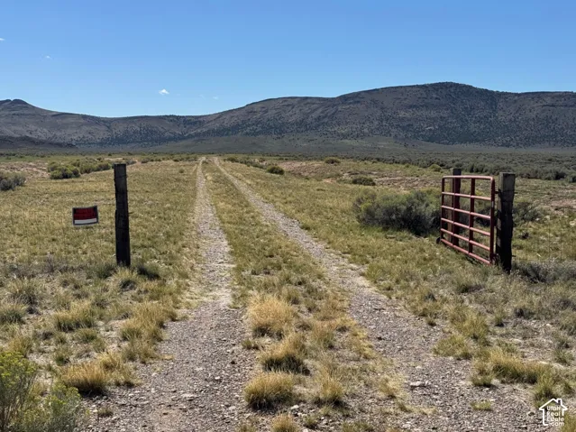 Expansive land parcel featuring a gravel path, a rustic metal gate, natural vegetation, and a distant mountain range