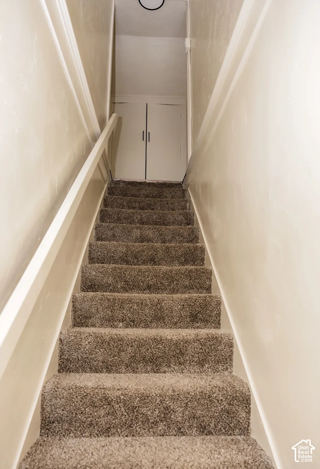 Carpeted staircase with a white handrail and light-colored wall paint