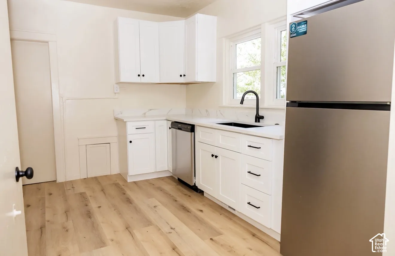 White shaker-style cabinetry with matte black hardware, quartz countertops, a stainless steel dishwasher, a black undermount sink with a matte black faucet, and wood-finish flooring