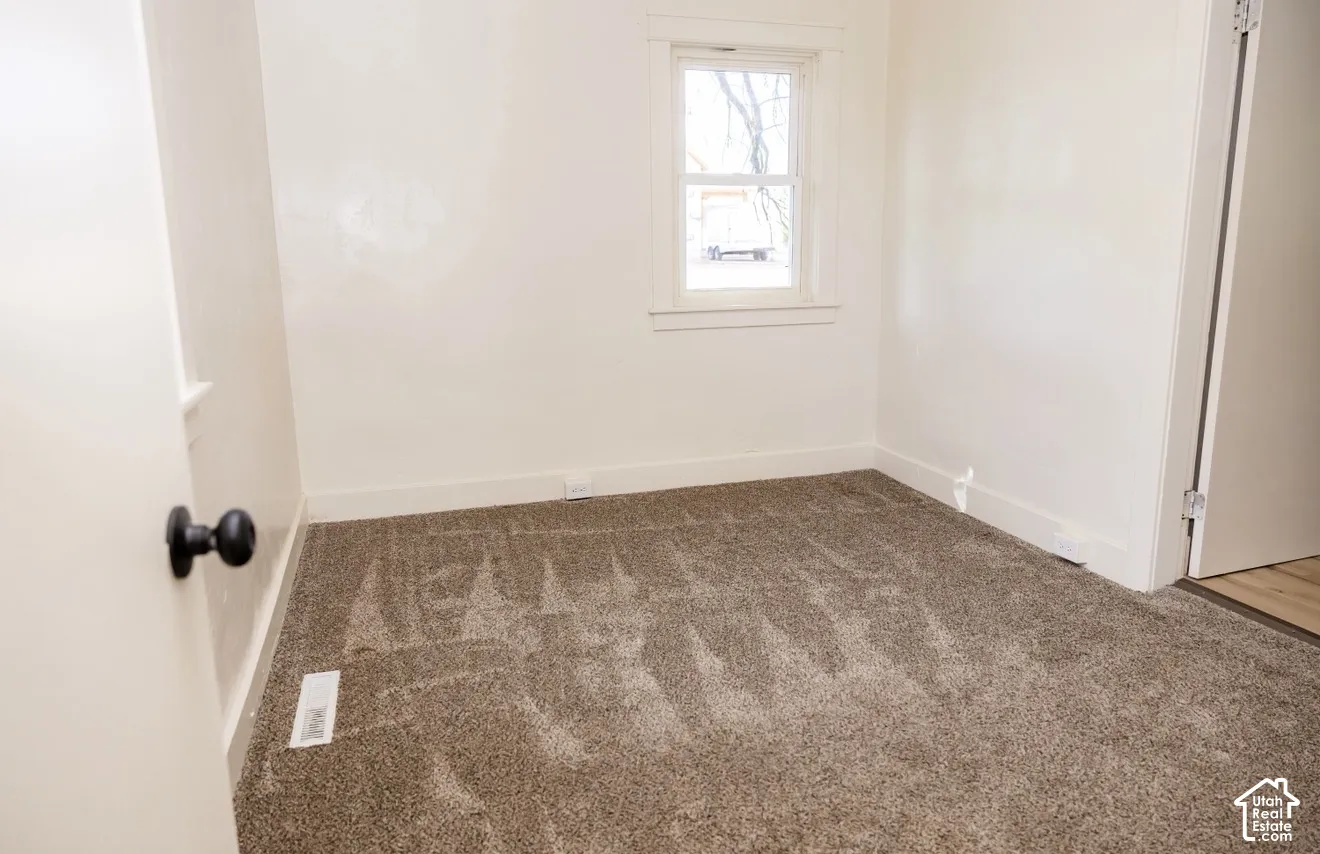 Carpeted flooring, white painted walls, and a single window with white trim