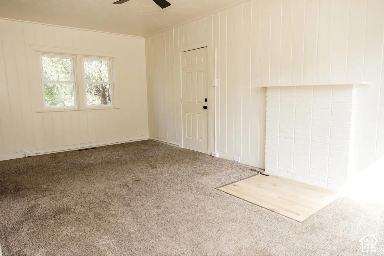 Light-filled interior featuring two windows, vertical paneling, and a white brick fireplace with a wood-finish hearth