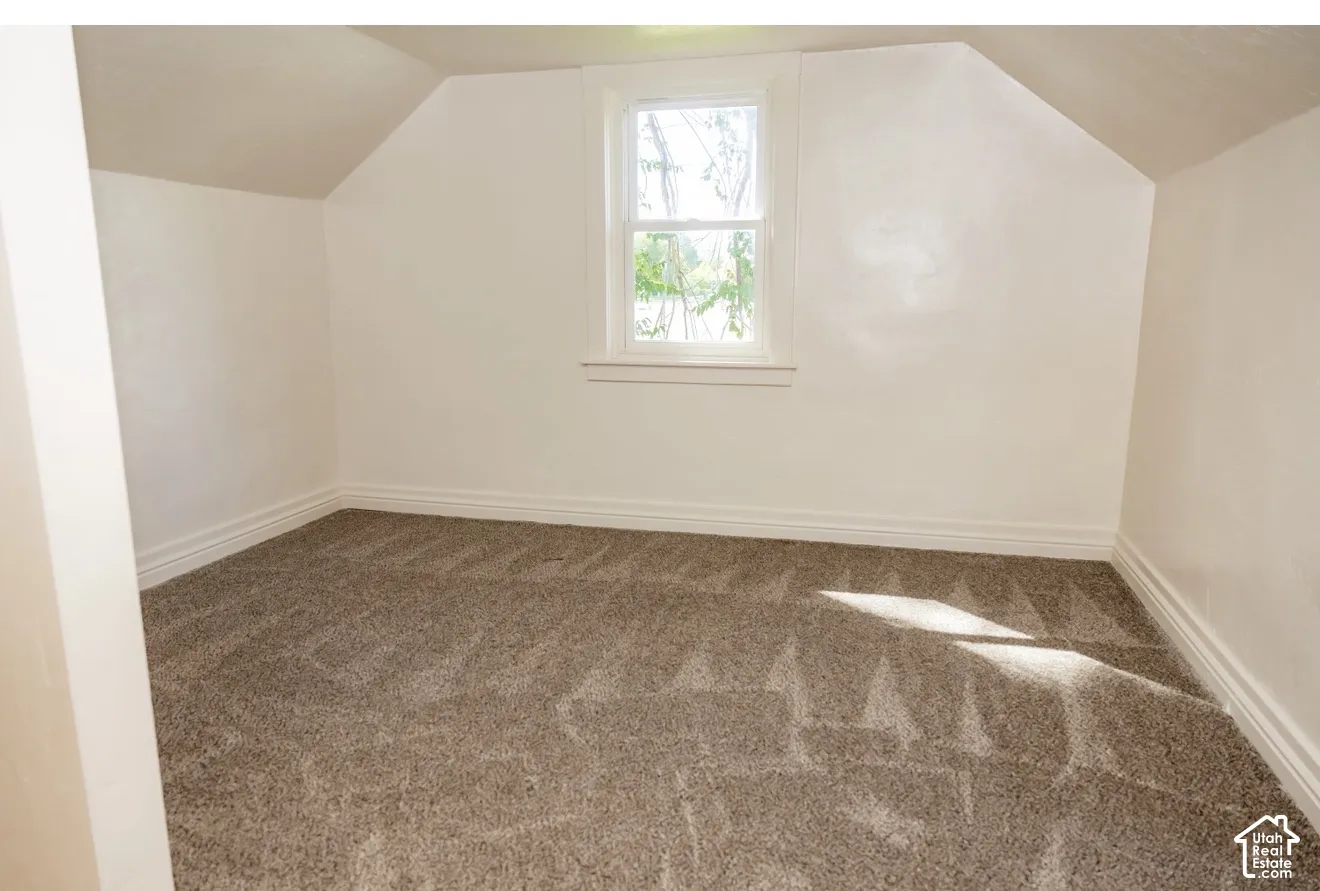 Attic room with sloped ceilings, white walls, a single pane window, and carpeted flooring
