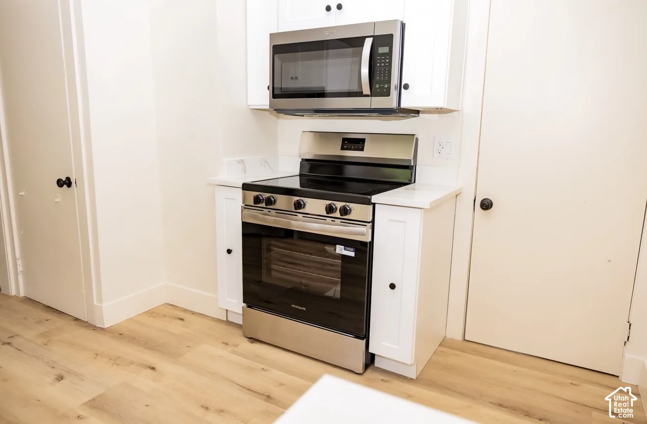 Stainless steel range with a built-in microwave, white upper and lower cabinetry, white countertops, and wood-finish flooring