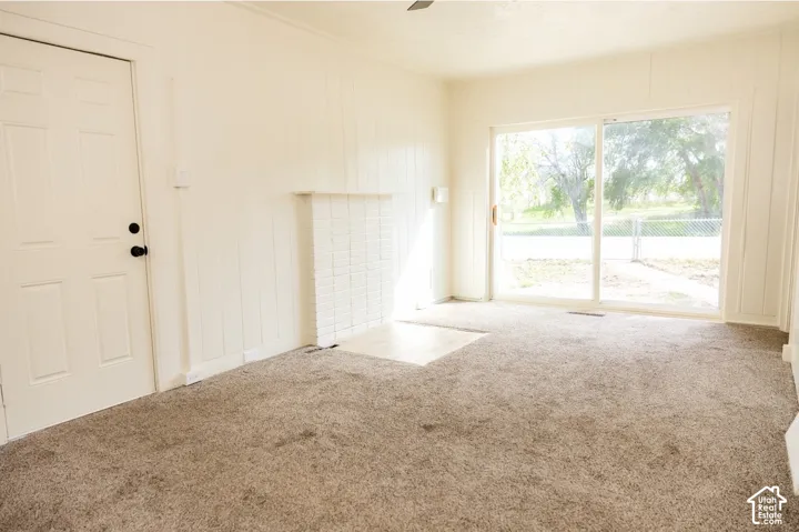 Carpeted interior space featuring a white painted brick fireplace with a hearth, a sliding glass door, and a paneled entry door