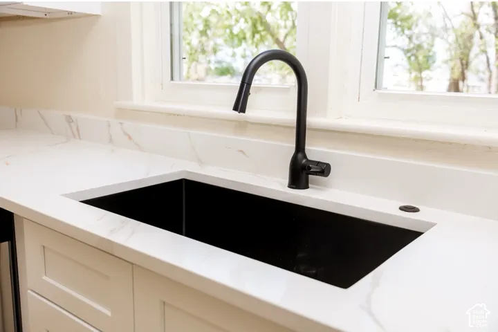 Single basin sink with a matte black gooseneck faucet, set within a white countertop featuring subtle veining, framed by white cabinetry