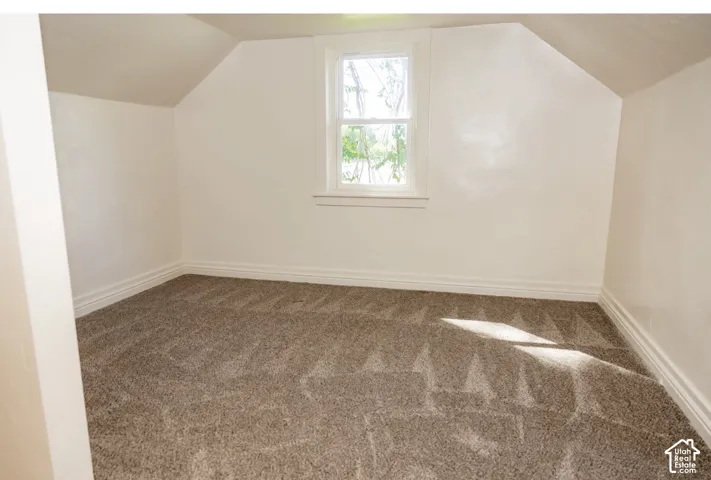 Attic room with sloped ceilings, white walls, a single pane window, and carpeted flooring