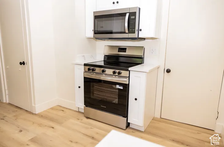 Stainless steel range with a built-in microwave, white upper and lower cabinetry, white countertops, and wood-finish flooring