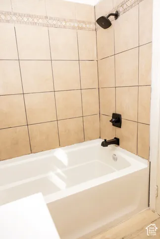 White bathtub with matte black fixtures, surrounded by tiled walls featuring a decorative mosaic accent band