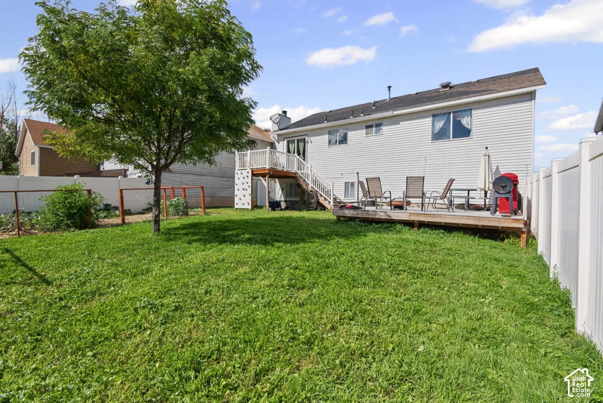 Expansive backyard featuring a mature tree, privacy fencing, and a multi-level wood deck with white railings