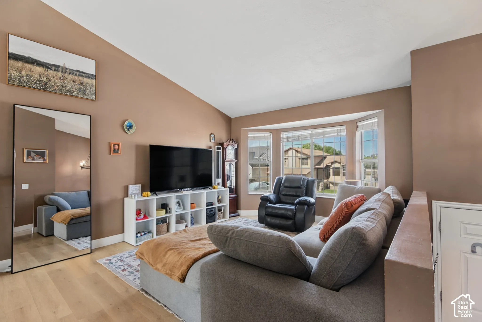 Vaulted ceiling, bay window, light wood-finish flooring, built-in shelving unit, and warm wall tones