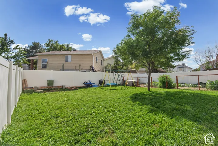 Expansive grassy yard featuring a mature tree, perimeter fencing, and a garden area