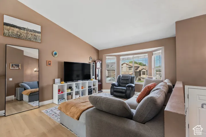 Vaulted ceiling, bay window, light wood-finish flooring, built-in shelving unit, and warm wall tones
