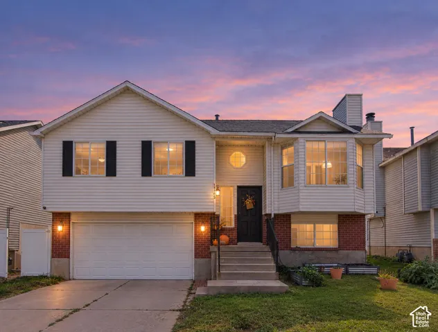 Split-level exterior featuring light-toned horizontal siding, a lower-level red brick facade, a multi-pane bay window, an attached two-car garage, and concrete steps leading to the front entrance