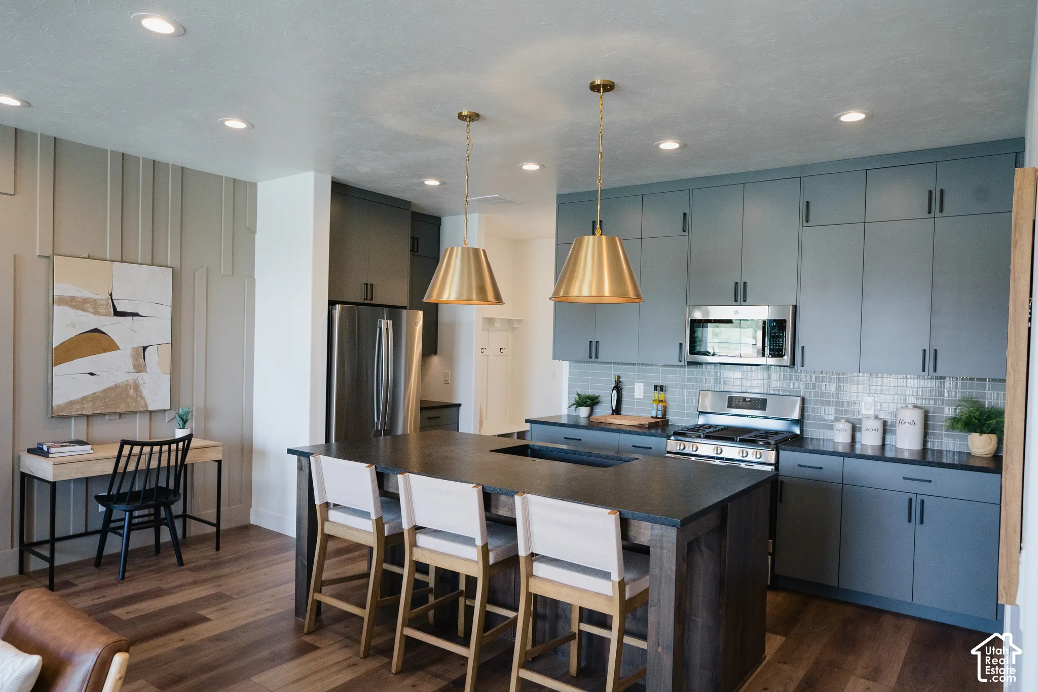 Wood-finish flooring throughout, kitchen island with dark stone countertop, full suite of stainless steel appliances, blue cabinetry with dark hardware, and recessed lighting