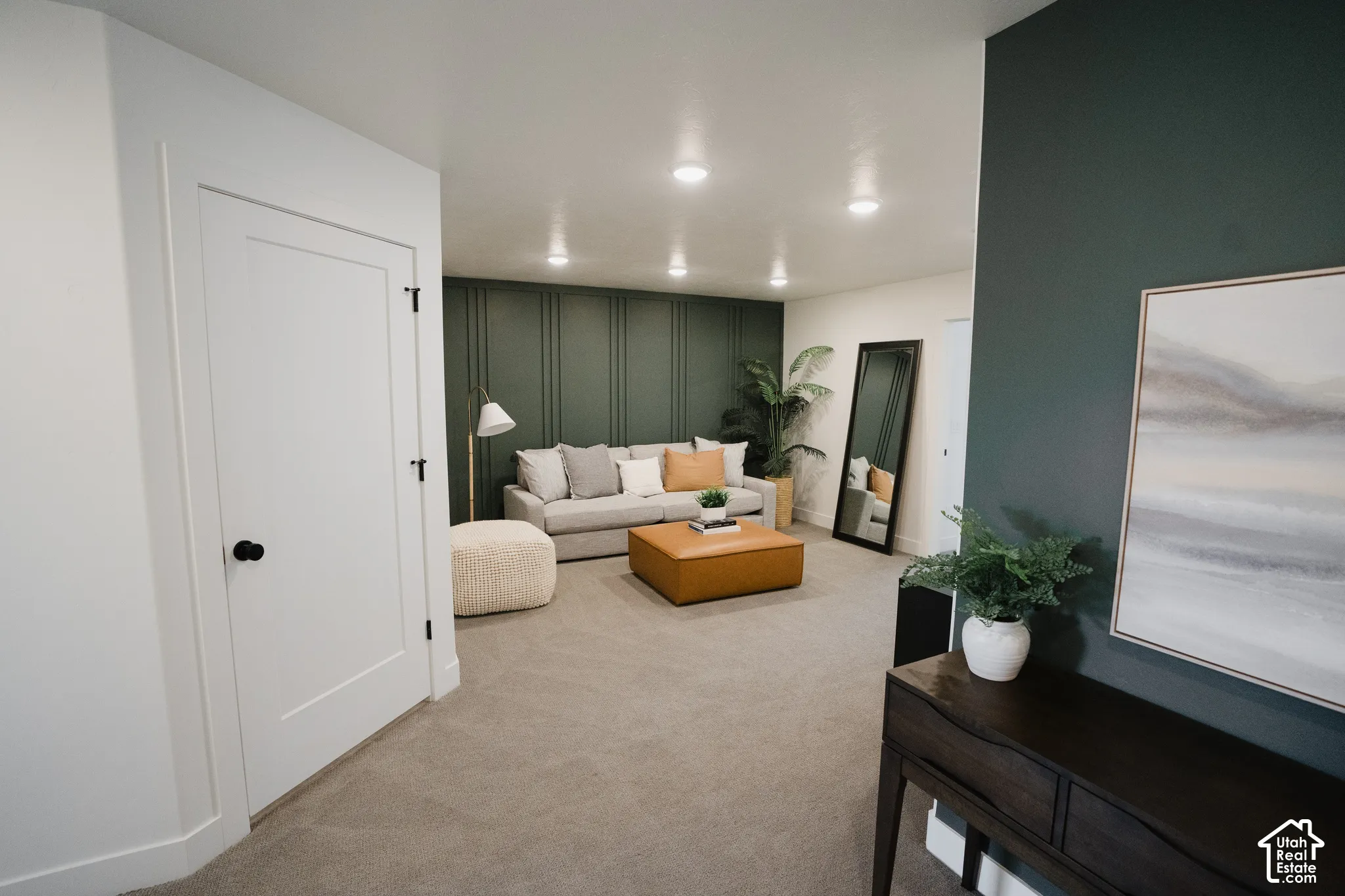 Recessed lighting illuminates a spacious room featuring a dark green accent wall with vertical paneling