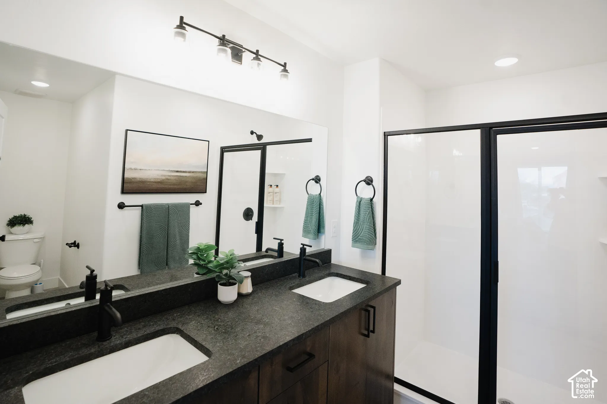 Dual vanity with dark wood-finish cabinetry and undermount sinks, stone-look countertop, black plumbing fixtures, and a shower with a black-framed glass enclosure
