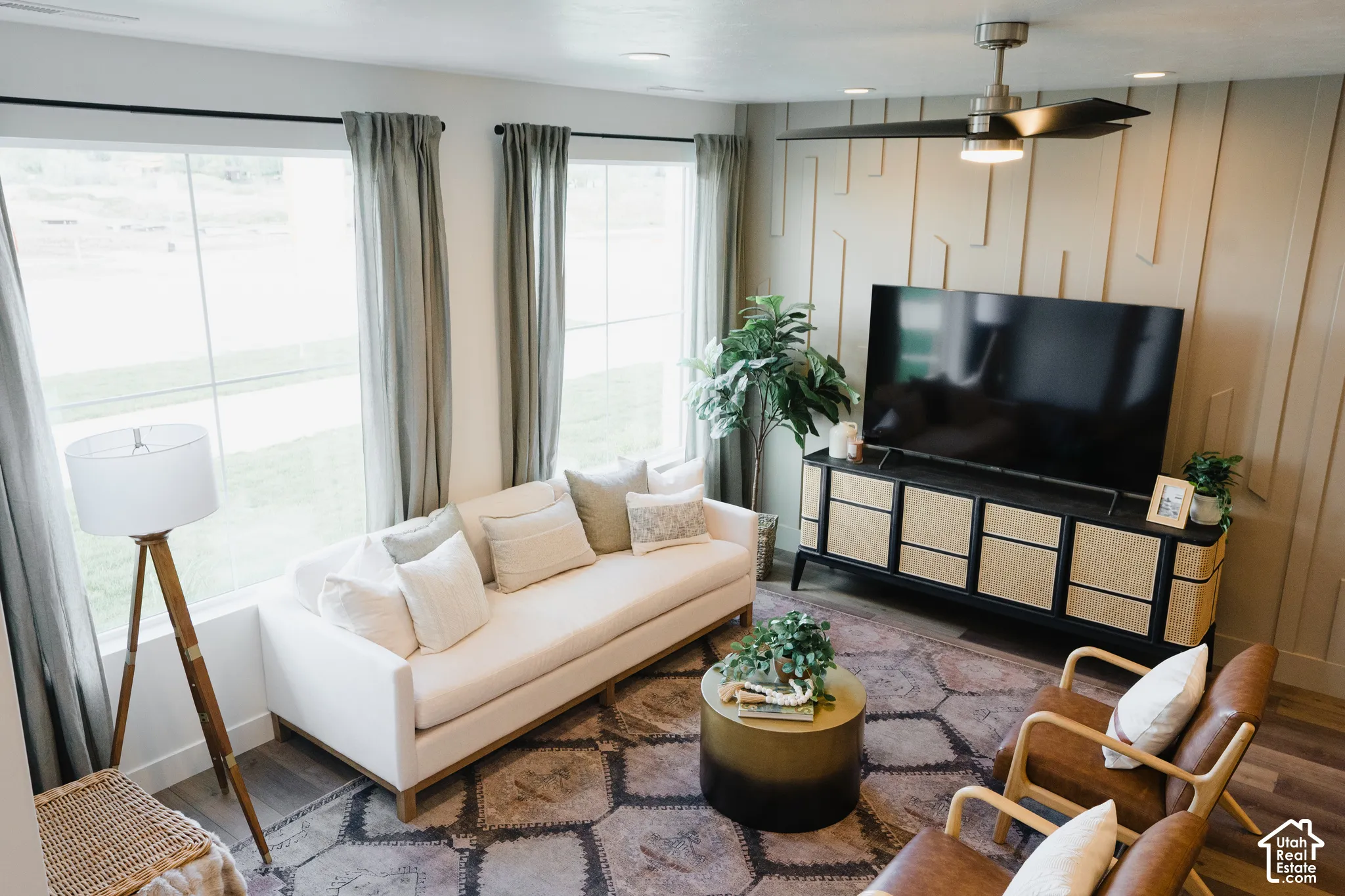 Wood-finish flooring, accent wall paneling, large windows, and a ceiling fan with integrated lighting