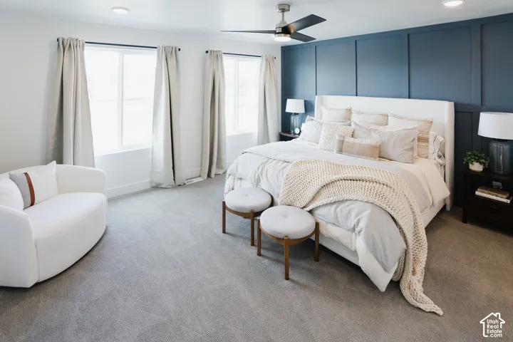 Recessed lighting, ceiling fan, accent wall with vertical paneling, light gray carpeting, and multiple windows