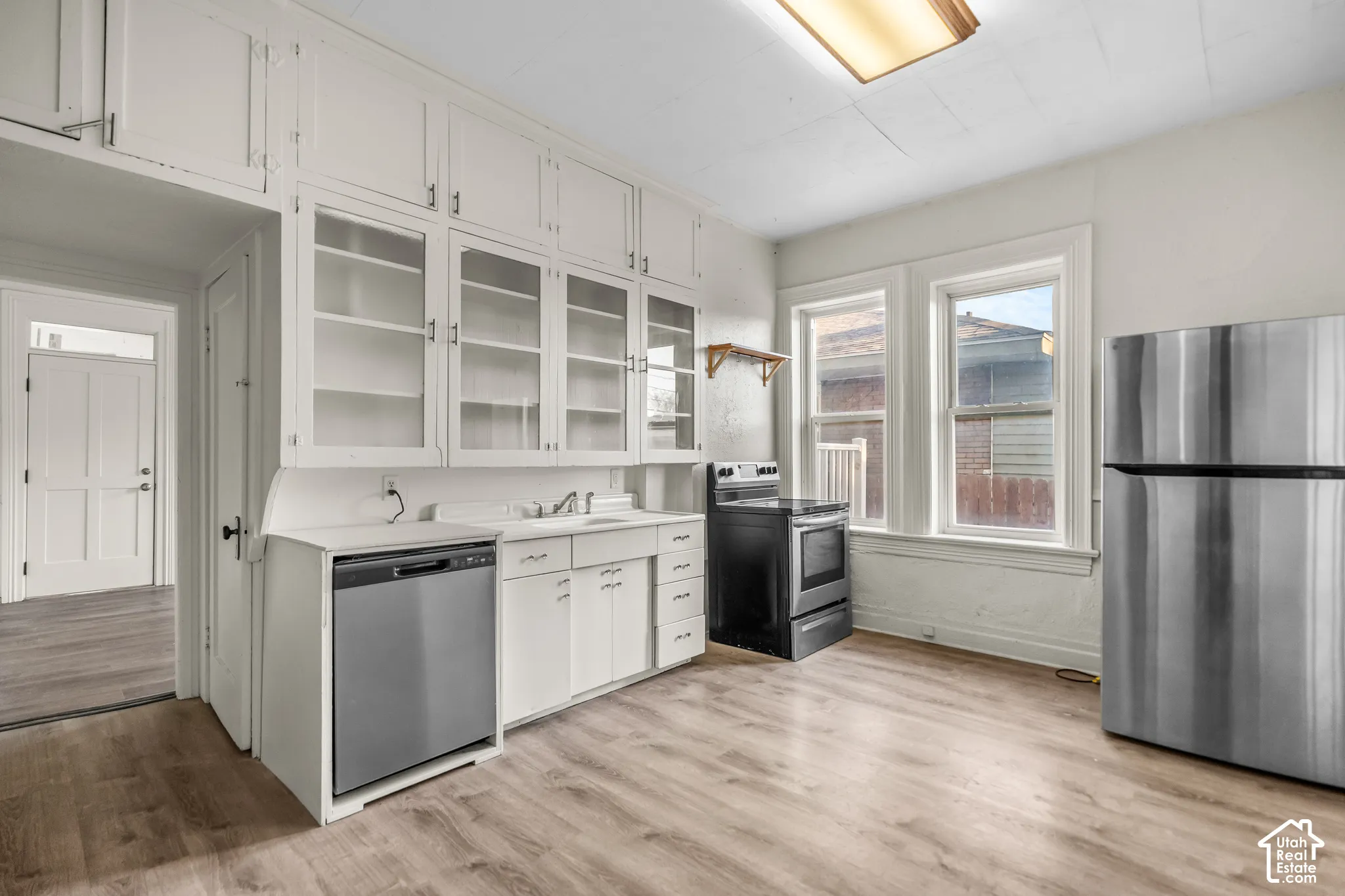 Kitchen featuring wood-finish flooring, white cabinetry, a stainless steel refrigerator, a black range, and a stainless steel dishwasher