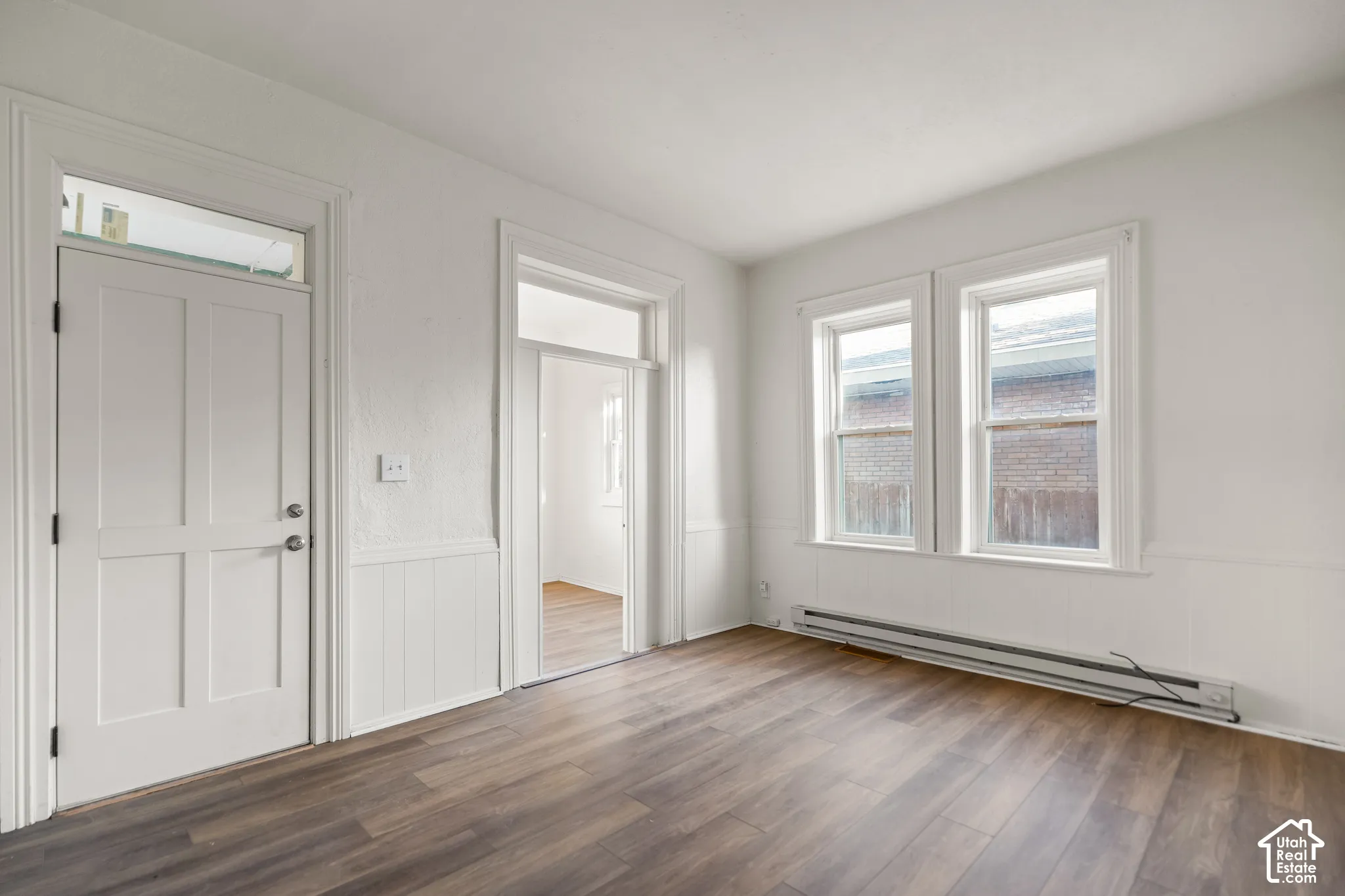 Wood-finish flooring, white paneled door with transom window, white wainscoting, and double windows with white trim