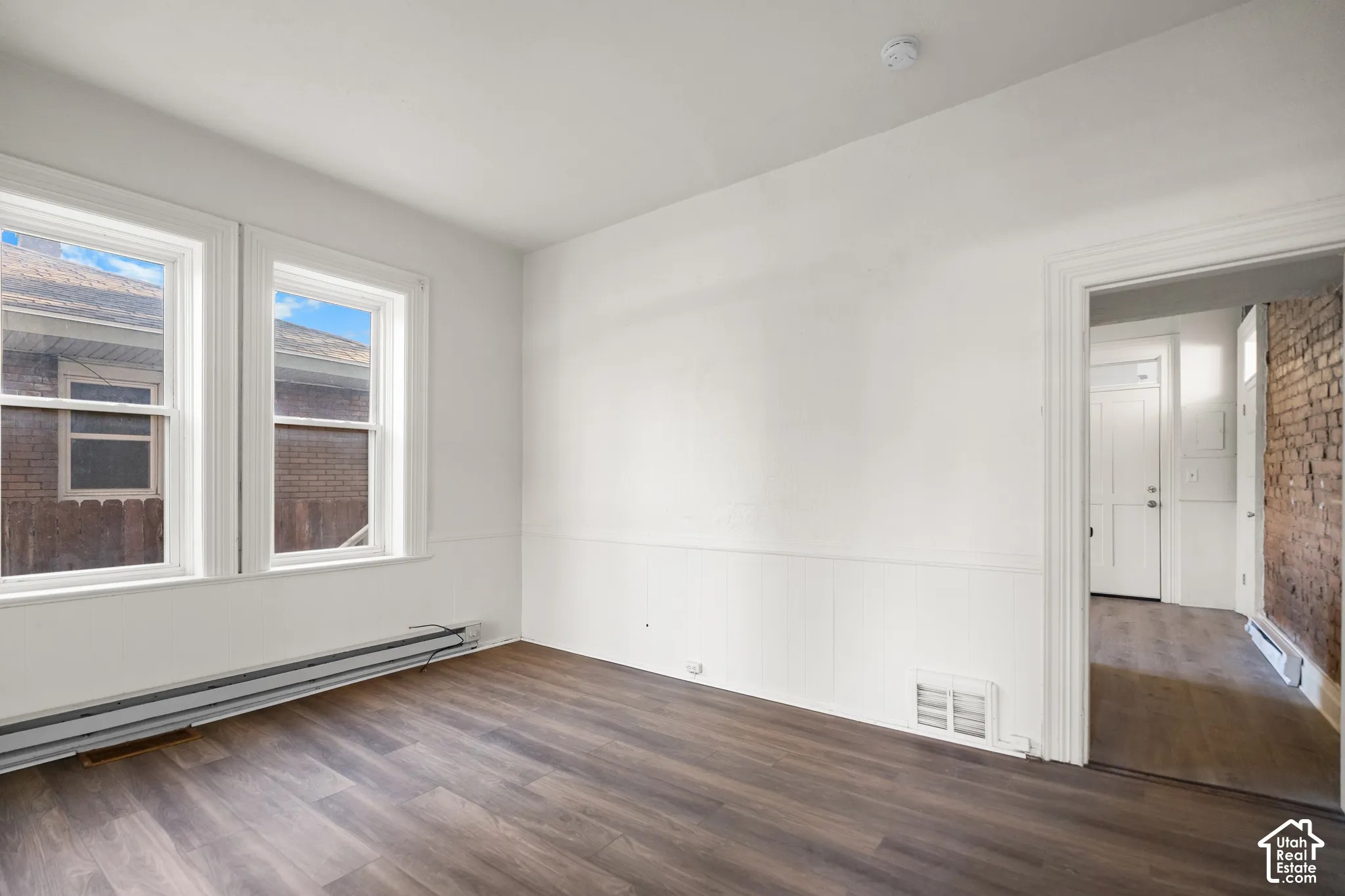 Wood-finish flooring, white paneled wainscoting, and two large windows