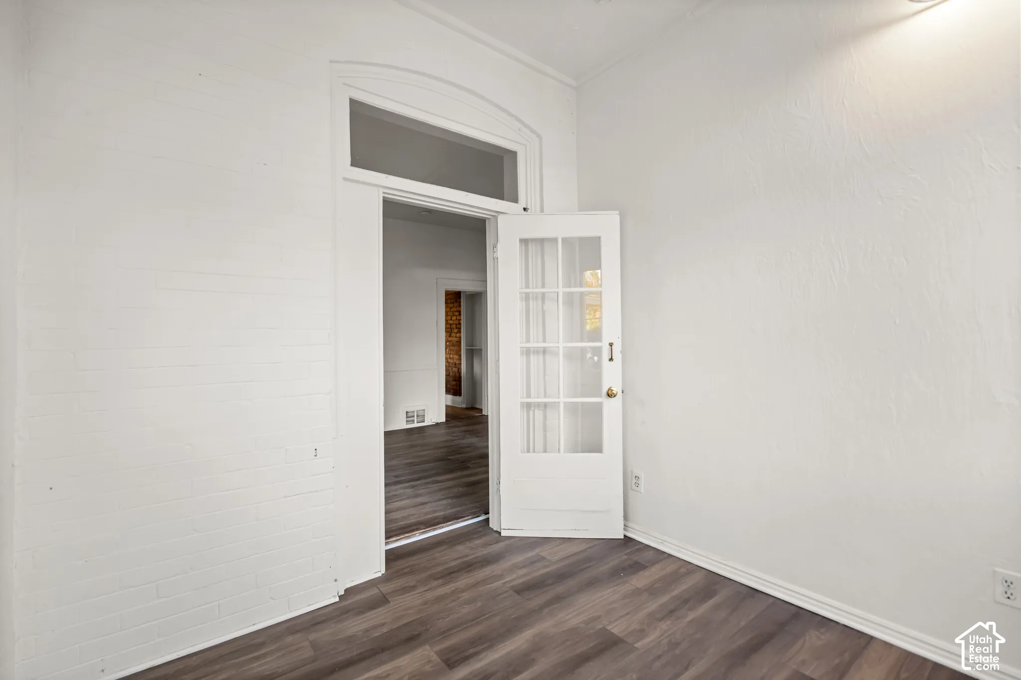 Wood-finish flooring, white painted brick accent wall, and a french door with arched transom