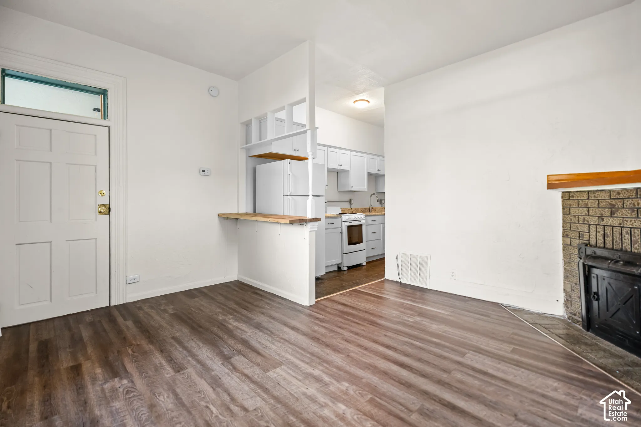 Wood-finish flooring throughout, bright white walls, and a brick fireplace