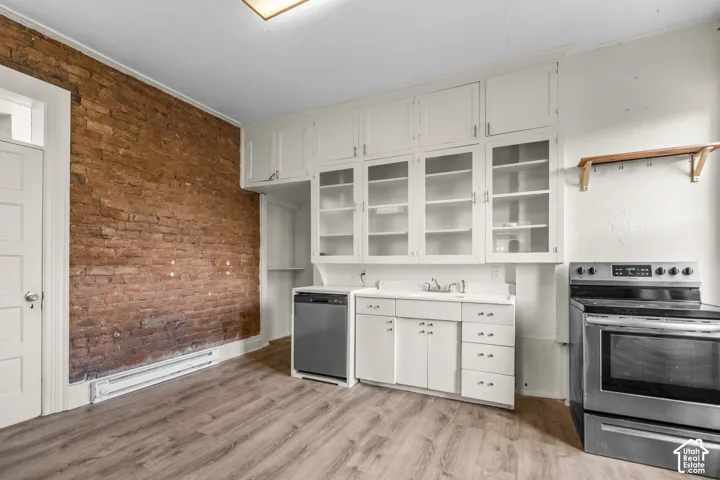 Exposed brick wall, wood-finish flooring, white cabinetry, built-in dishwasher, and stainless steel range